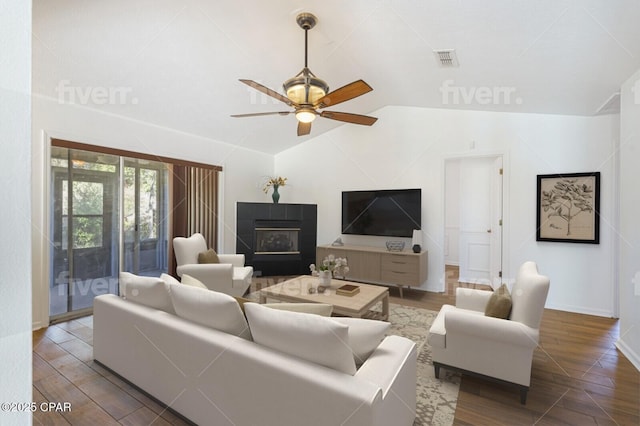 living room with a tiled fireplace, visible vents, vaulted ceiling, and wood finished floors