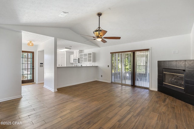 unfurnished living room featuring dark wood-style flooring, a healthy amount of sunlight, and a tiled fireplace