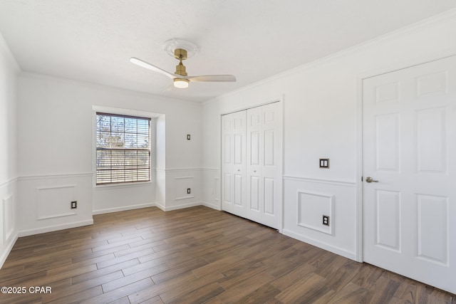 unfurnished bedroom with a wainscoted wall, a closet, dark wood finished floors, and crown molding