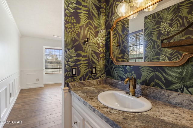 bathroom featuring a wainscoted wall, wood finished floors, vanity, wallpapered walls, and crown molding