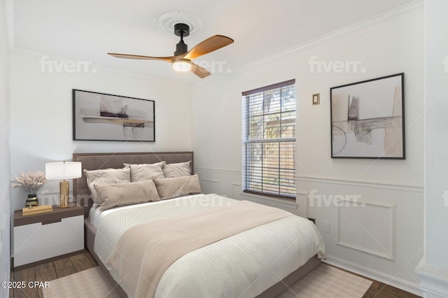 bedroom featuring a wainscoted wall, a decorative wall, ornamental molding, ceiling fan, and wood finished floors