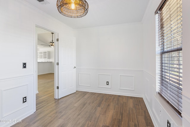 empty room with ceiling fan, ornamental molding, wood finished floors, and a decorative wall