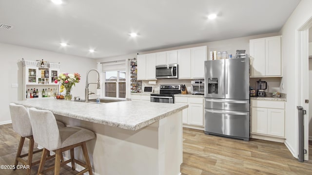 kitchen featuring light countertops, appliances with stainless steel finishes, white cabinetry, a sink, and an island with sink