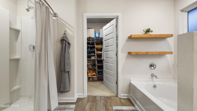 bathroom with a bath, a shower stall, a walk in closet, and wood finished floors