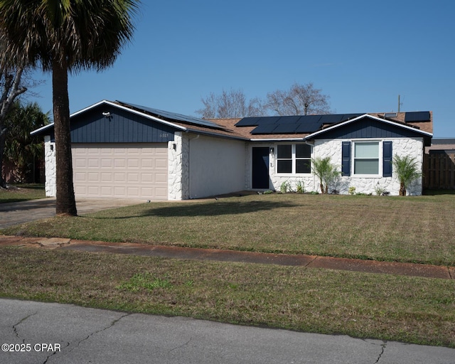 view of front of home featuring an attached garage, solar panels, driveway, stone siding, and a front yard