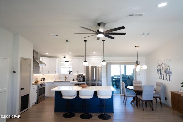kitchen featuring visible vents, wall chimney exhaust hood, a kitchen island, stainless steel appliances, and light countertops