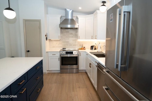 kitchen featuring white cabinets, decorative backsplash, wall chimney exhaust hood, stainless steel appliances, and a sink