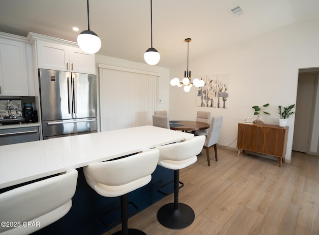 kitchen featuring a breakfast bar, visible vents, light wood-style flooring, freestanding refrigerator, and white cabinetry