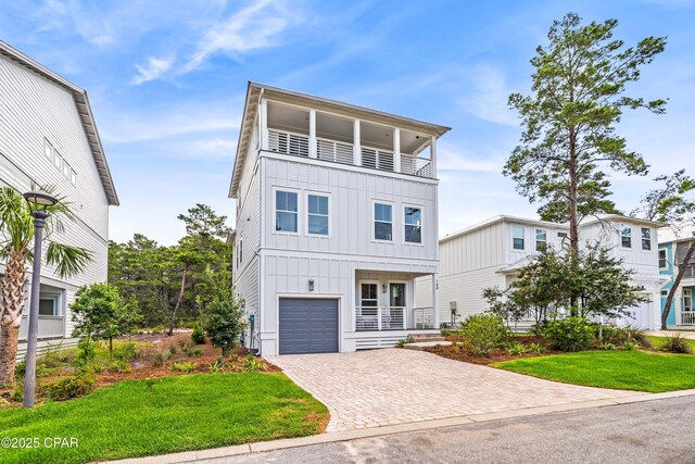 coastal home featuring a balcony, decorative driveway, a front lawn, and board and batten siding