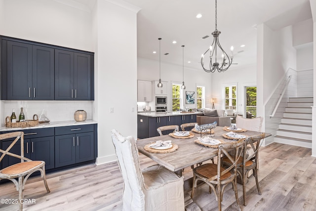 dining space with light wood-style floors, a towering ceiling, an inviting chandelier, and stairs