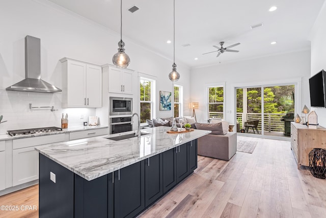 kitchen with open floor plan, white cabinets, hanging light fixtures, and wall chimney range hood