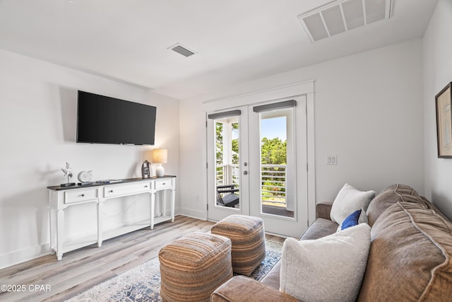 living area featuring light wood finished floors, baseboards, visible vents, and french doors