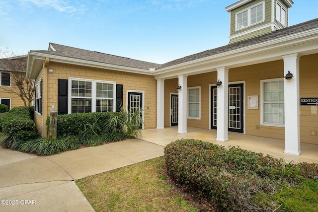 doorway to property with covered porch and a shingled roof