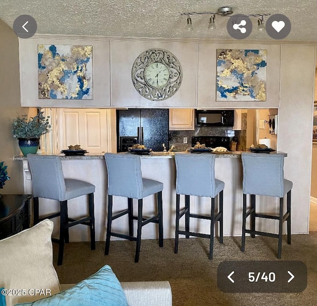 kitchen with black appliances, tasteful backsplash, a kitchen bar, and a textured ceiling