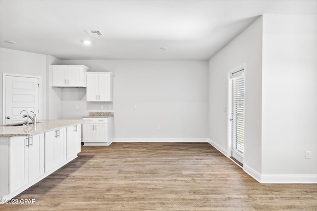 kitchen with light wood finished floors, baseboards, light stone countertops, white cabinetry, and a sink