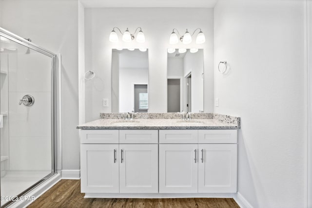 bathroom with double vanity, a shower stall, wood finished floors, and a sink