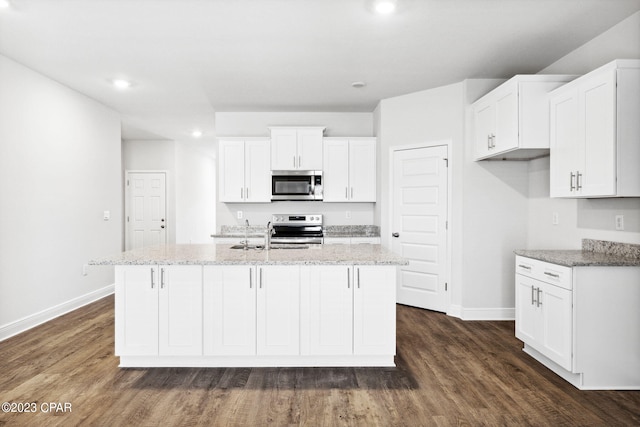 kitchen with light stone countertops, an island with sink, white cabinets, stainless steel appliances, and dark wood-style flooring