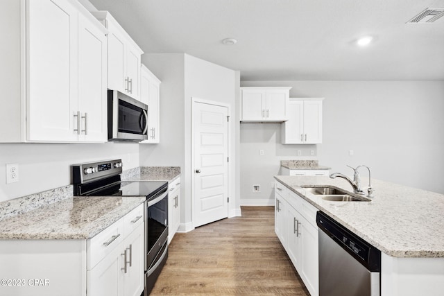 kitchen featuring visible vents, a center island with sink, light wood-style flooring, stainless steel appliances, and a sink