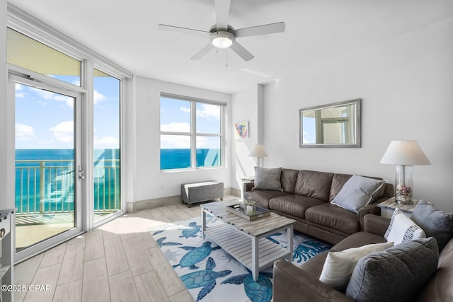 living room with ceiling fan, light wood-type flooring, a water view, and baseboards