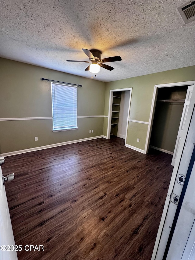 unfurnished bedroom with dark wood-style floors, multiple closets, visible vents, a textured ceiling, and baseboards