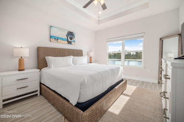 bedroom featuring a ceiling fan, baseboards, a tray ceiling, light wood finished floors, and crown molding