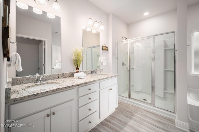 bathroom with double vanity, wood finished floors, a sink, a shower stall, and a bath