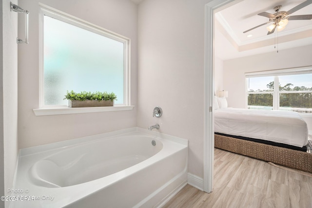 ensuite bathroom with a tray ceiling, crown molding, ensuite bath, wood finished floors, and a bath