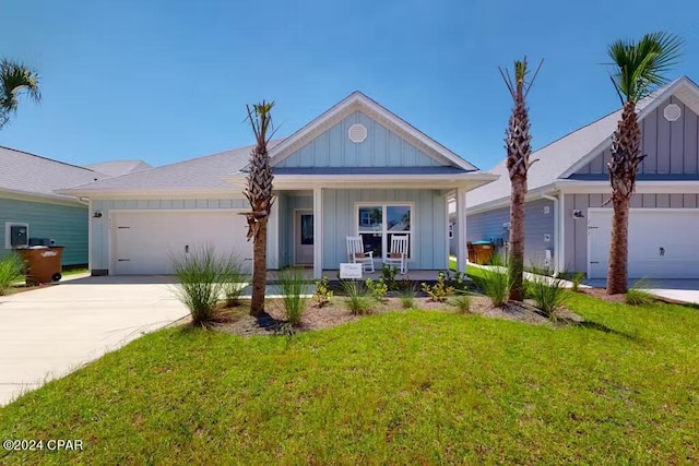 view of front of property featuring covered porch, board and batten siding, a garage, driveway, and a front lawn