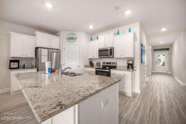 kitchen featuring appliances with stainless steel finishes, white cabinetry, a sink, a kitchen island with sink, and light wood-type flooring