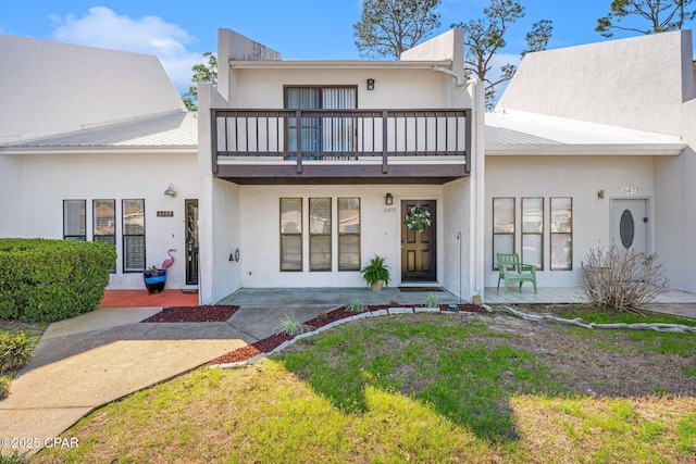 townhome / multi-family property with metal roof, a front lawn, a balcony, and stucco siding