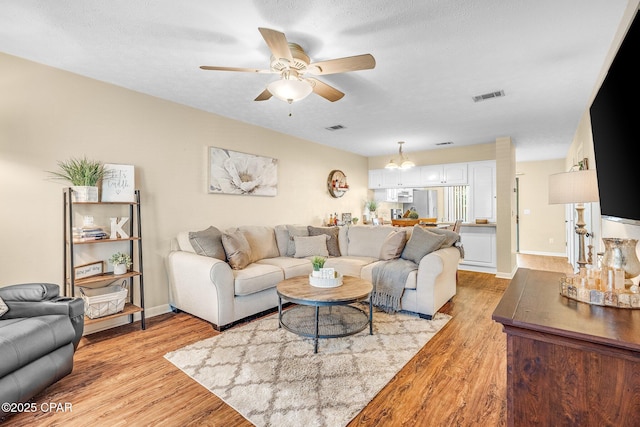 living room with light wood-style flooring, visible vents, ceiling fan, and a textured ceiling