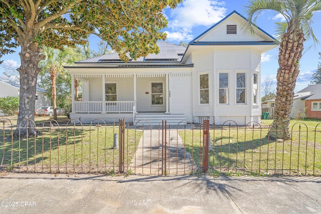 view of front of property featuring a porch, roof mounted solar panels, a fenced front yard, and a front lawn