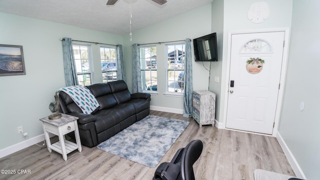 living area with ceiling fan, a textured ceiling, baseboards, vaulted ceiling, and light wood-type flooring