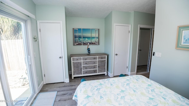 bedroom featuring access to exterior, a textured ceiling, baseboards, and wood finished floors