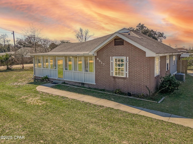 view of front of property featuring a shingled roof, a lawn, a sunroom, cooling unit, and brick siding