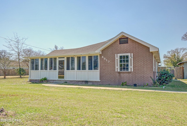 view of front of house featuring a sunroom, fence, a front lawn, and brick siding