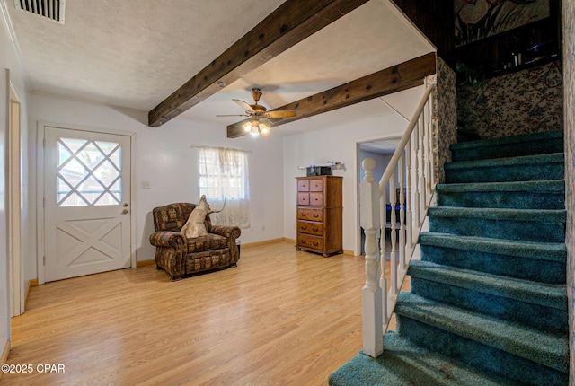 living area featuring beam ceiling, visible vents, light wood-style flooring, a textured ceiling, and stairs