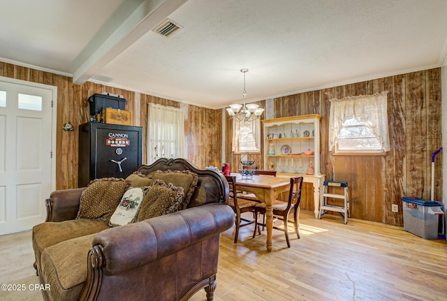 living area with beam ceiling, light wood finished floors, visible vents, ornamental molding, and a chandelier