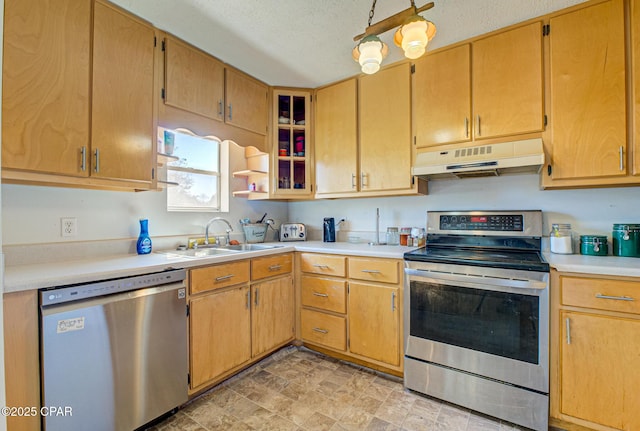 kitchen with appliances with stainless steel finishes, light countertops, a textured ceiling, under cabinet range hood, and a sink