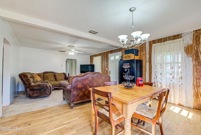 dining room featuring visible vents, beamed ceiling, light wood-type flooring, wood walls, and ceiling fan with notable chandelier