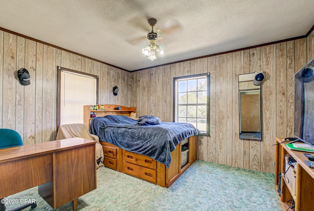 carpeted bedroom featuring crown molding, wooden walls, a ceiling fan, and a textured ceiling