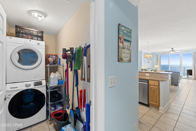 clothes washing area with a ceiling fan, laundry area, light tile patterned flooring, stacked washer and clothes dryer, and a textured ceiling