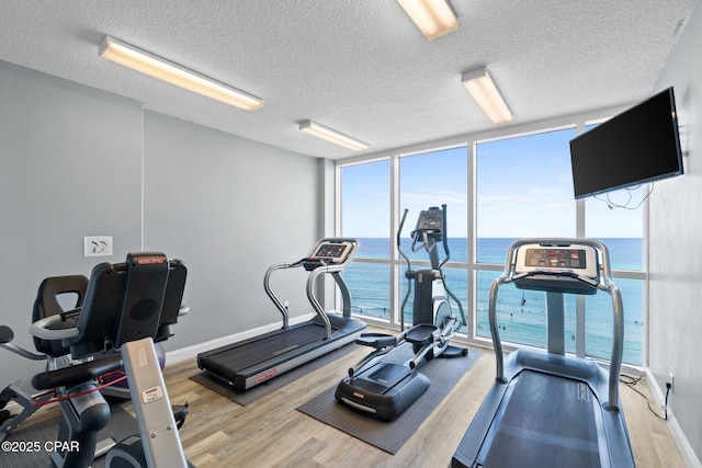 exercise room featuring expansive windows, baseboards, a textured ceiling, and wood finished floors