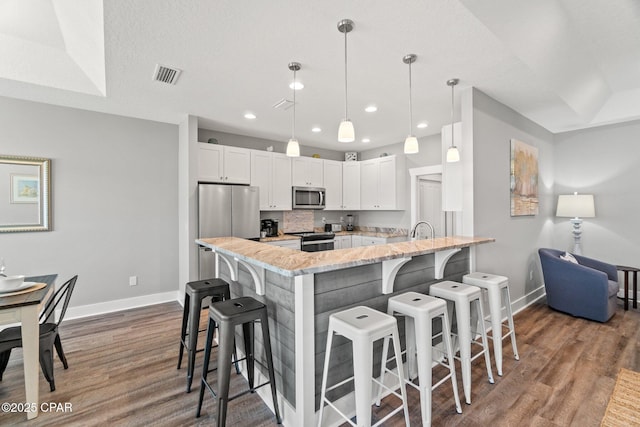 kitchen with hanging light fixtures, appliances with stainless steel finishes, white cabinetry, a peninsula, and a kitchen bar