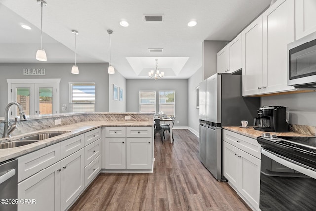 kitchen featuring stainless steel appliances, white cabinets, a sink, and decorative light fixtures