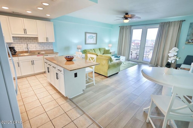 kitchen featuring a breakfast bar, a sink, a kitchen island, white cabinetry, and decorative backsplash
