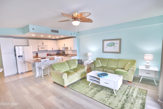 living room with light wood-type flooring, visible vents, and a ceiling fan