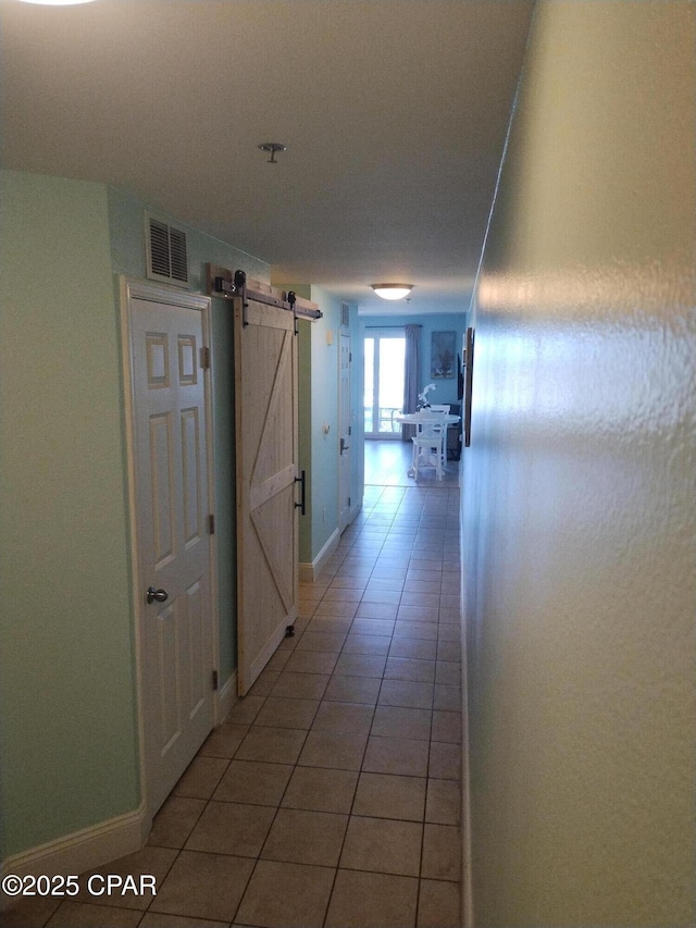 corridor featuring light tile patterned floors, a barn door, visible vents, and baseboards