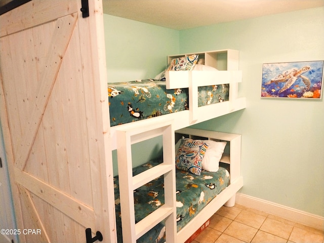 tiled bedroom featuring a barn door and baseboards