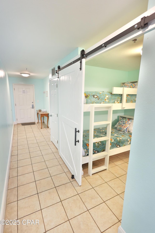 hallway featuring tile patterned floors, a barn door, baseboards, and visible vents